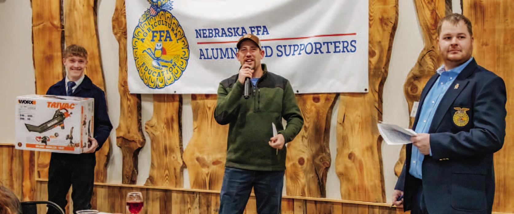 Garret Cumbow presenting an auction item while Travis Connot encourages the group to bid. President of the FFA Alumni Chapter Matt Scholz.