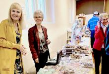 Ladies behind the Bazaar table making sales are Nancy Isom and her sister, Shari McMullen. Opposite, in line to eat, is Vada Haumann, member of Thedford UCC.