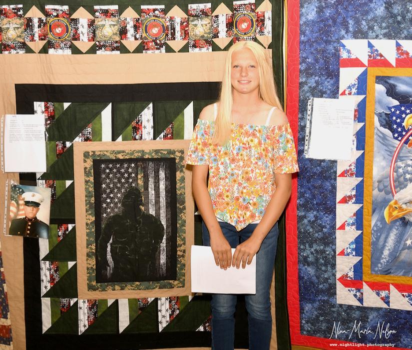 Christen Larson – Malard standing in front of the Quilt of Valor she crafted for Jason Parks.