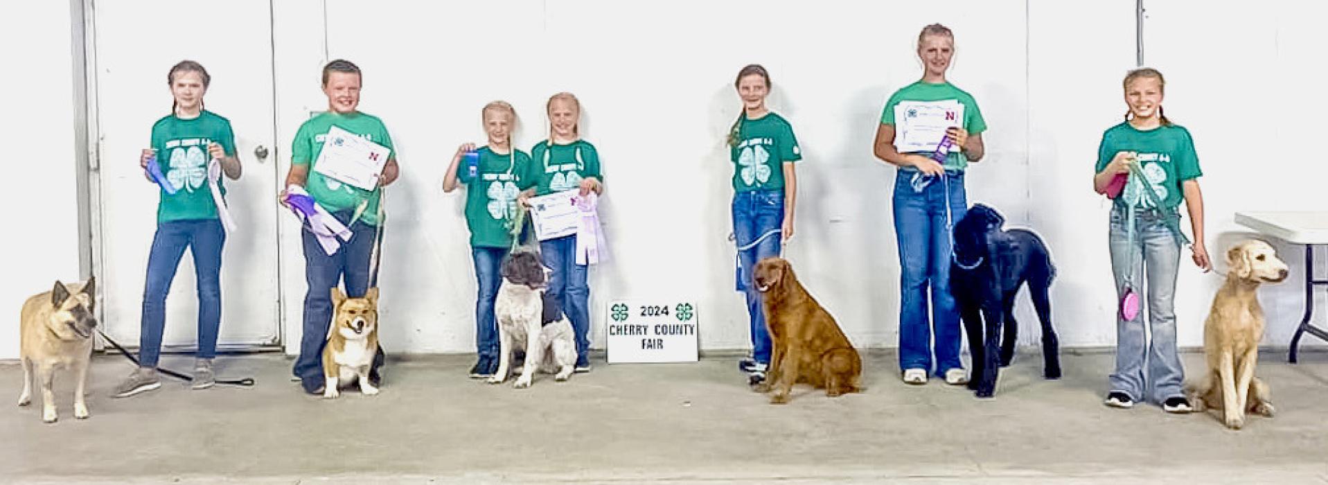 2024 Dog Show participants are pictured from L to R: Elise Brown, Henry Johnson, Kimber Burge, Marlie Burge, Chloe Christiansen, Adalin Wickman, and Sarah Burge.