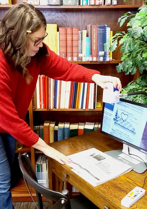 Librarian Carrie Graham demonstrates how the video magnifier works with last week’s edition of the Valentine Midland News. Not only can it focus downward, but the camera she’s positioning with her left hand, can be adjusted to focus outward across a room for example. Photo by Laura Vroman